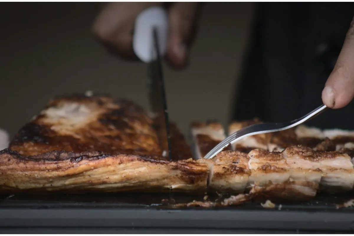 Roast pork with crackling being carved with a knife and fork