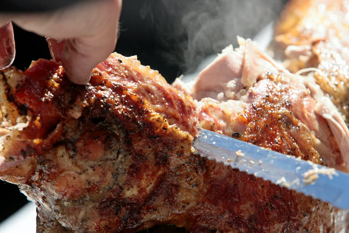 A knife carving slices from a roast pork joint