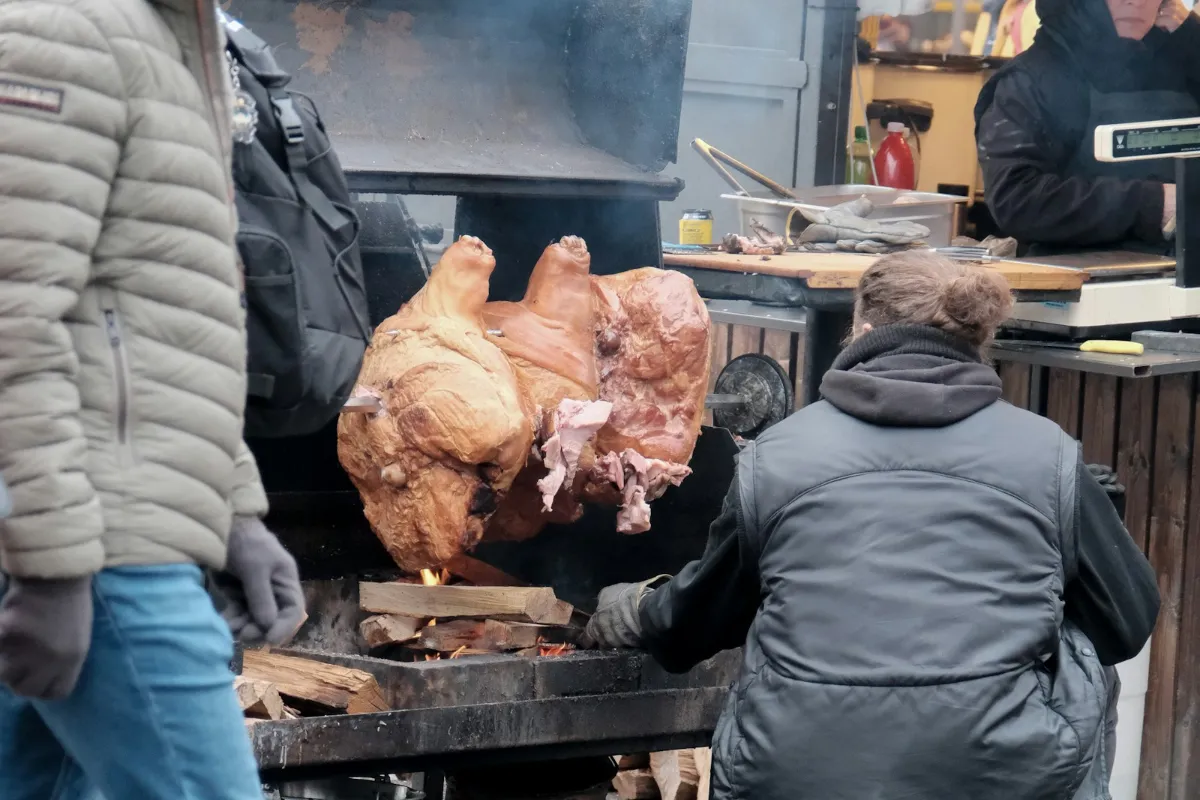 A whole pig roasting outdoors on a cold day, with people in coats nearby