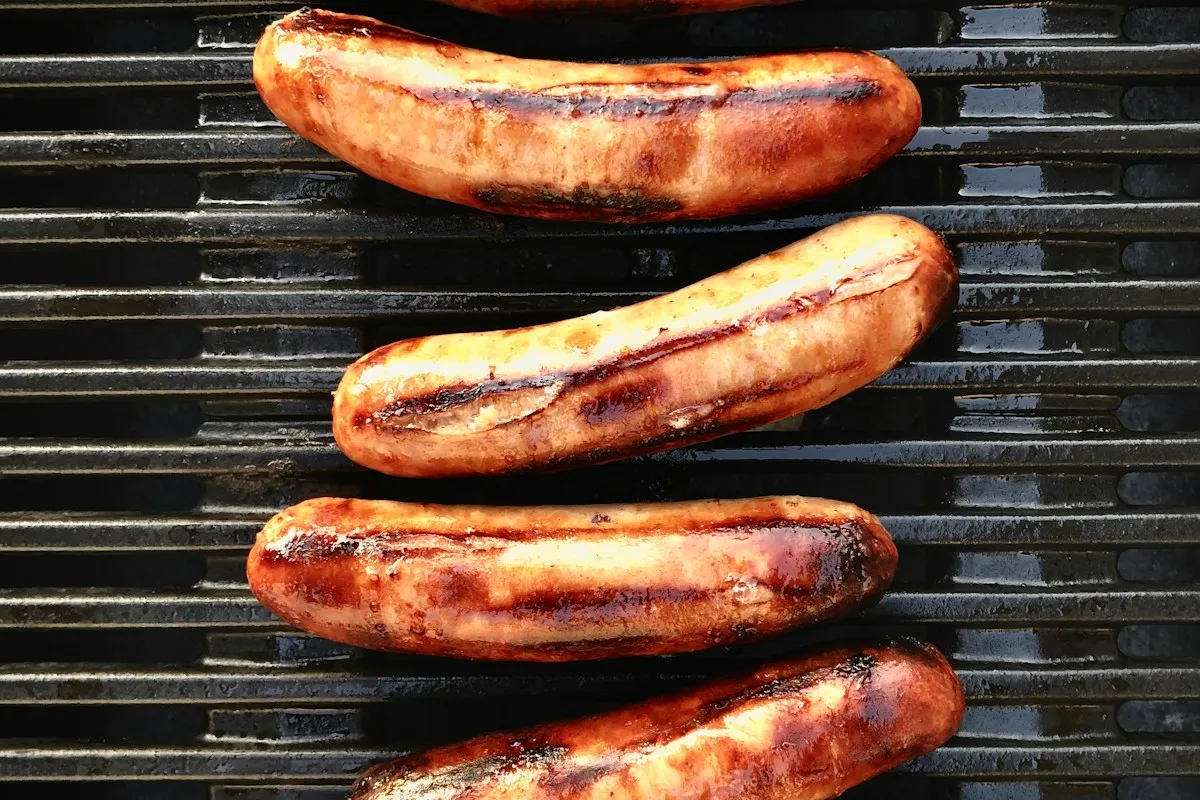 Four browned sausages on a barbecue grill