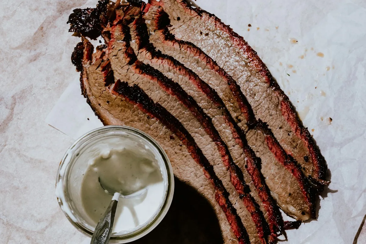 Slices of barbecued beef brisket with a pot of sauce